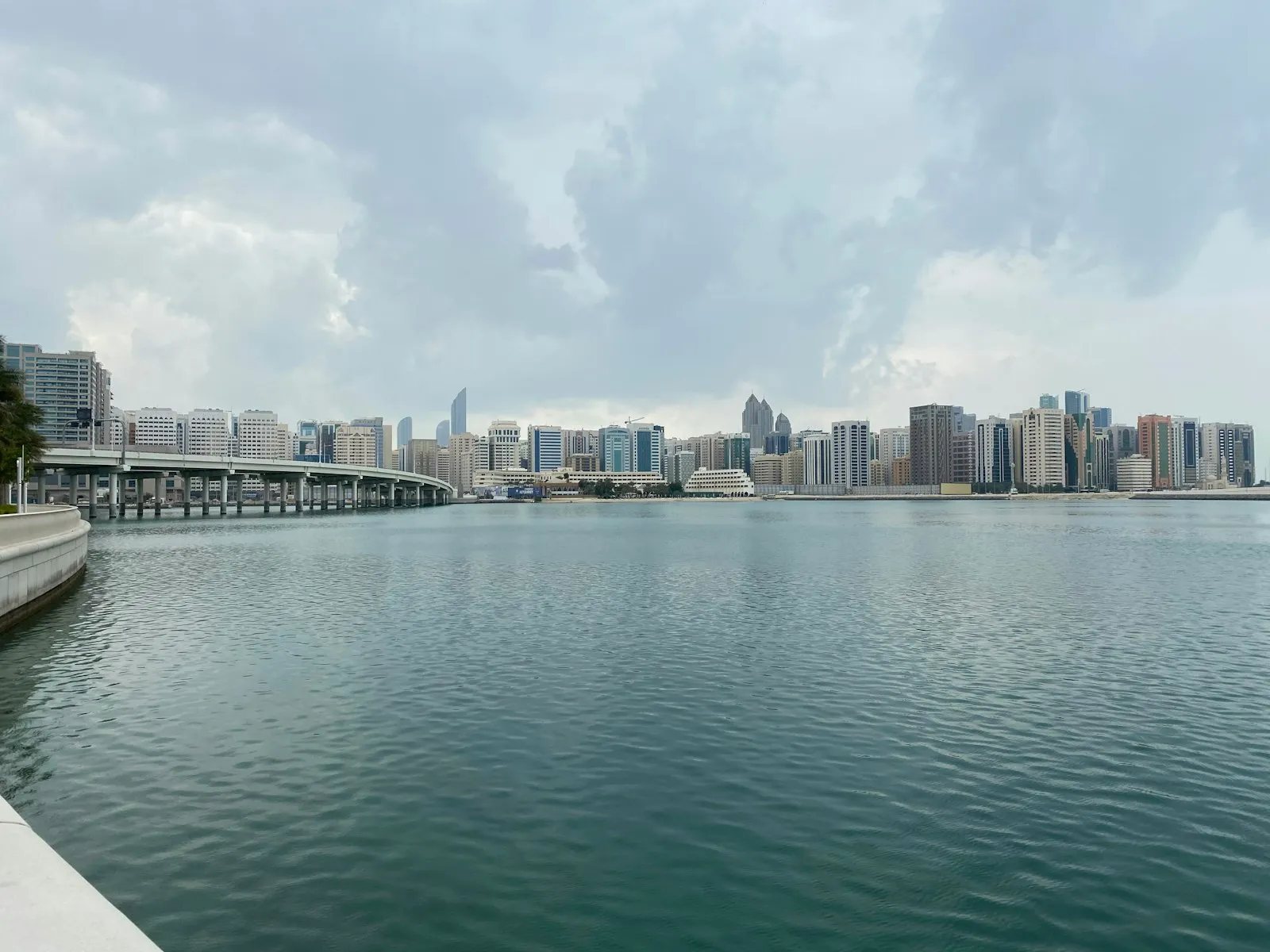 The Abu Dhabi skyline across the water on an overcast day, with a curving causeway on the left