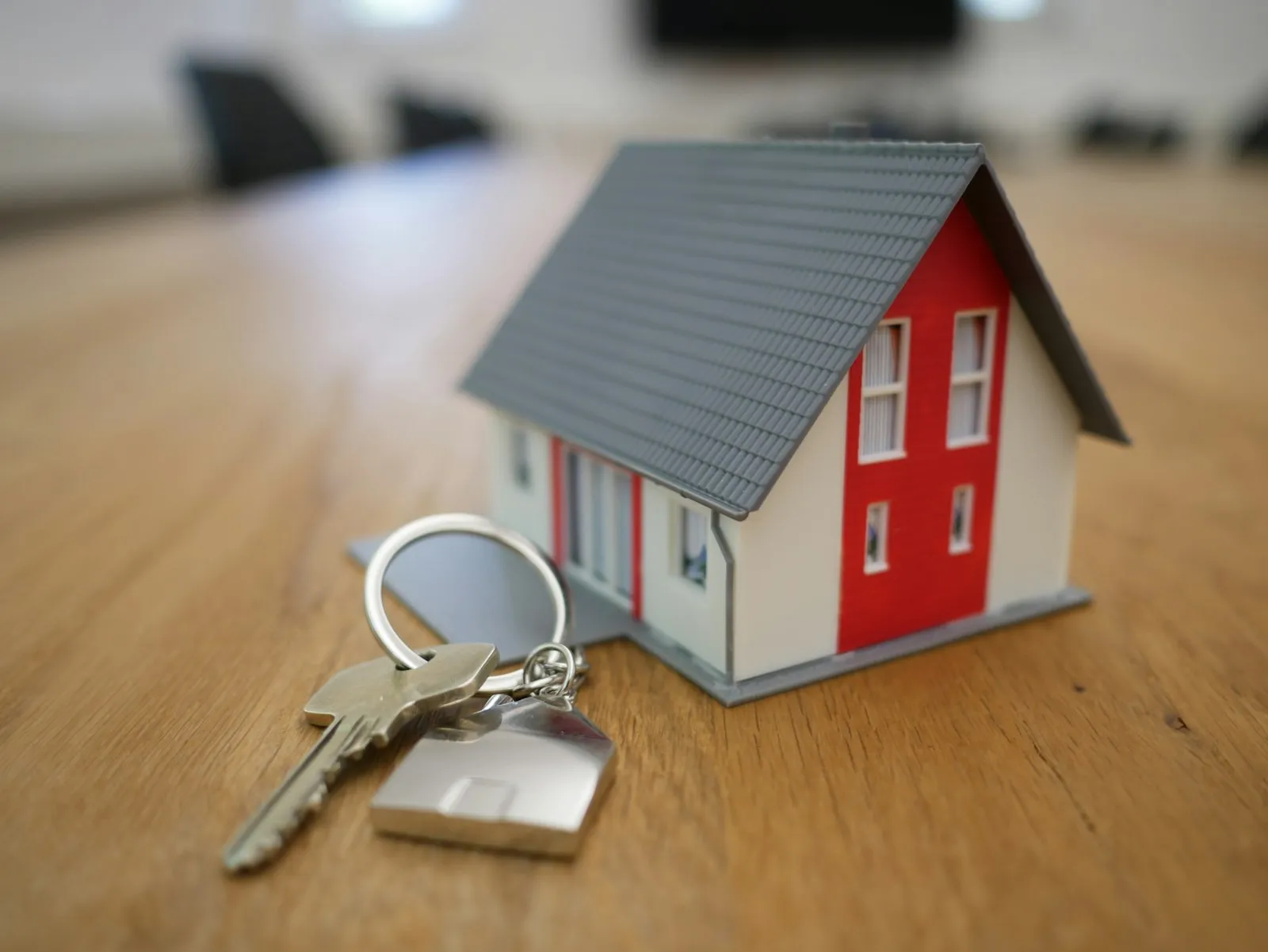 A small model house and a set of keys on a wooden desk