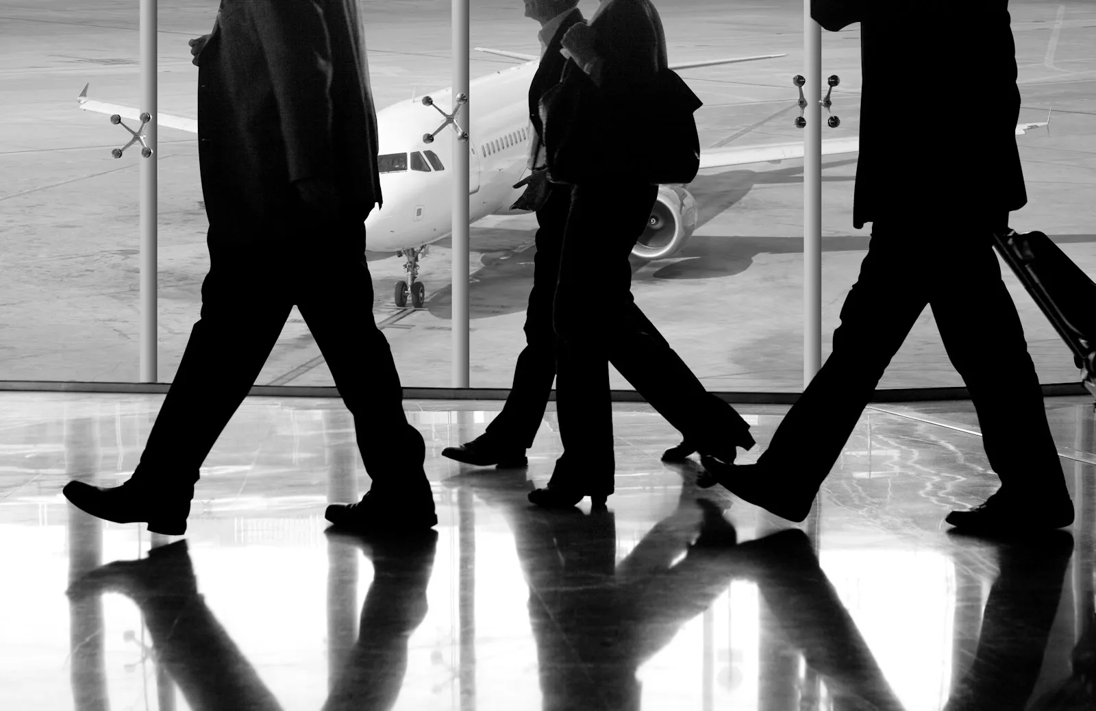 Business travellers walking through an airport terminal, a plane visible behind glass