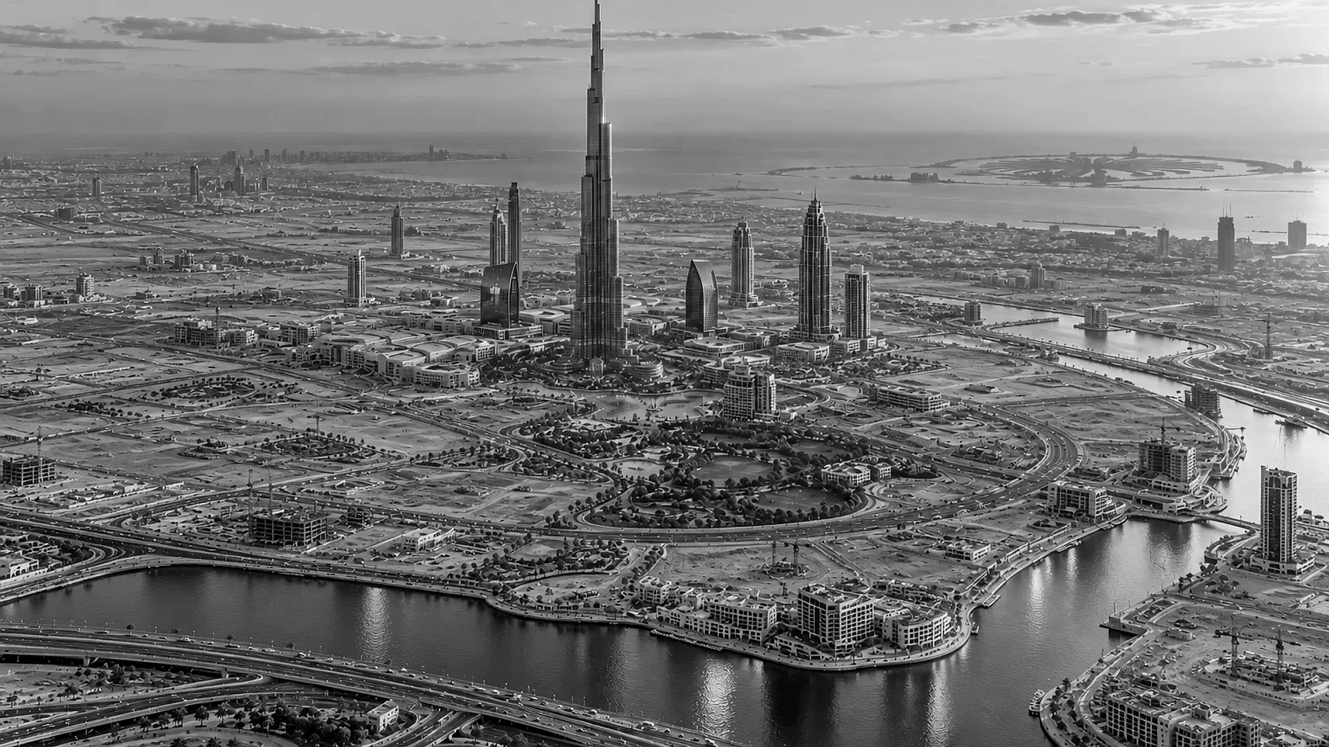 The Burj Khalifa and Downtown Dubai towers above parks, a lake and the Dubai Water Canal with a busy highway: a finished community