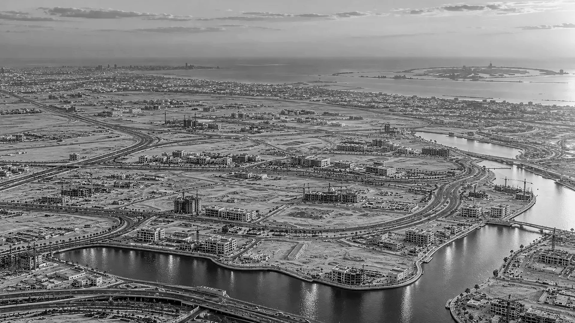 New communities under construction along a canal, with cranes, curving roads and the Palm Jumeirah on the coast: development following the roads