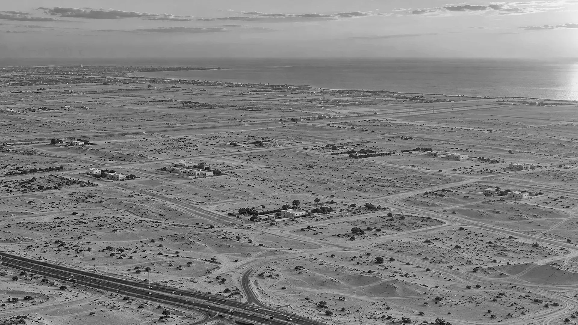 The same desert coast with a highway and its first link roads laid across the sand and a few walled villas: infrastructure arriving before the city